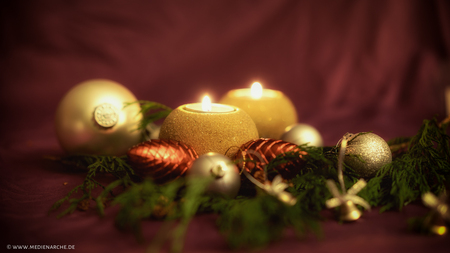 Weihnachtsbaumkugeln, Zapfen und Kerzen vor weichem roten Hintergrund, mit Immergrün.